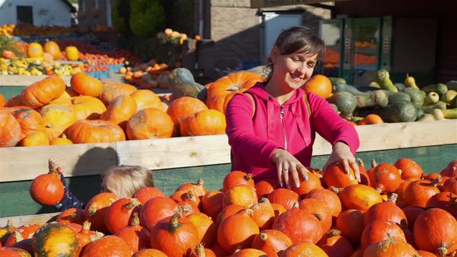 Little Girl with her Mother Buying Halloween Pumpkin at the Farmers Market in Sunny Autumn Day. Slow Motion. Halloween Harvesting and Thanksgiving Concept