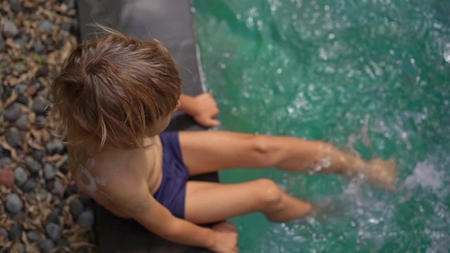 Slowmotion shot of a little boy with a sun drawn by a sunscreen cream on his shoulder splash water in a swimming pool. Sun protection concept