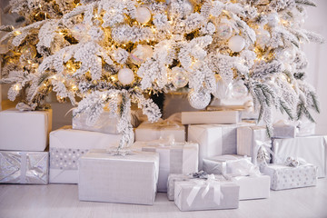 Christmas presents under New Year tree with artificial snow with golden illumination. Silver color
