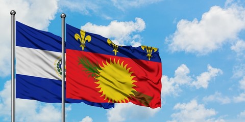 El Salvador and Guadeloupe flag waving in the wind against white cloudy blue sky together. Diplomacy concept, international relations.