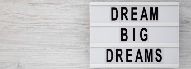 'Dream big dreams' words on a lightbox on a white wooden surface, top view. Overhead, from above, flat lay. Space for text.