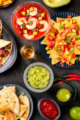 Mexican food, many dishes of the cuisine of Mexico, flatlay, top shot on a black background. Nachos, tequila, guacamole, shrimp cocktail, quesadillas
