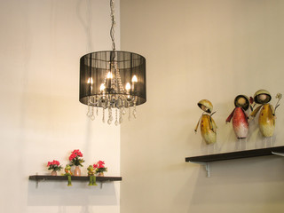A small black chandelier lightens up the corner of a white room decorated with dolls and artificial flowers