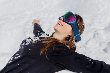 Fototapeta na wymiar Close up of a young happy woman tourist in ski goggles, posing lying on the snow in winter sunny day. Copy space.