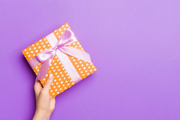Flat lay of woman hands holding gift wrapped and decorated with bow on purple background with copy...