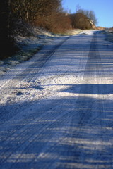 road coverd in a bit of snow, tyre marks and tracks and early morning shadows in beautiful blue colours