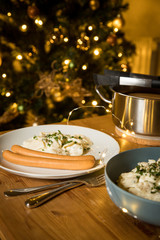 Wiener Würstchen und Kartoffelsalat als typisches Weihnachtsessen zu Heiligabend in Deutschland am Weihnachtsbaum mit Weihnachtsdekoration und Lichterketten