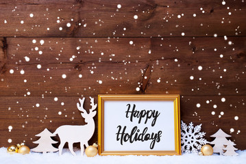 Frame With English Calligraphy Happy Holidays. Golden Decoration Like Ball, Tree And Deer. Wooden Background With Snow And Snowflakes