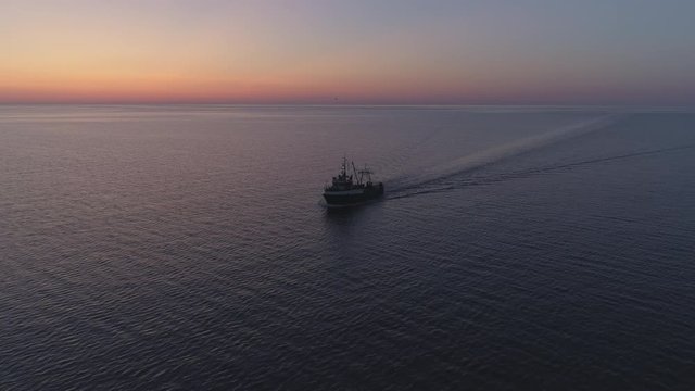 Fishing boat sailing on sea in summer night twilight after sunset aerial shot