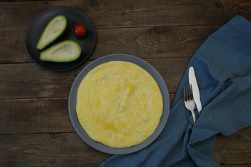 Omelette or omelet and avocado, tomato on the wooden rustic background with tissue napkin, fork and knife. Top view Flat lay. Photo for menu. Food background, pattern, poster. With copy space for text