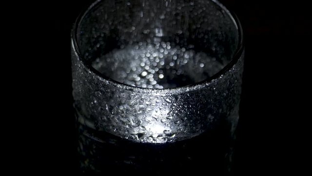 A wet glass of water spins in the dark and moves away