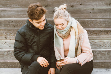 Loving teenagers on date look at mobile phones, girl shows guy something interesting on mobile...