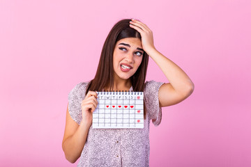 Young beautiful woman holding menstruation calendar over isolated background with surprise face....