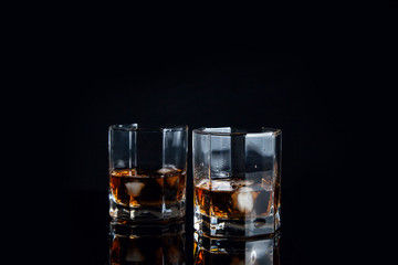 Two glasses of whiskey with ice isolated on black background..