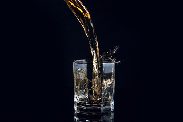 Whiskey pouring into glass with ice isolated on black background..