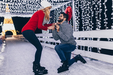Handsome man proposing a beautiful woman to marry him in ice skating rink.