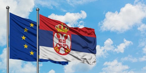 European Union and Serbia flag waving in the wind against white cloudy blue sky together. Diplomacy concept, international relations.