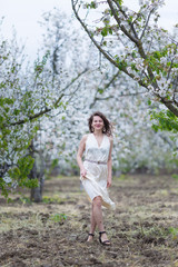 Naklejka premium Piękna młoda kobieta rasy kaukaskiej z ciemnymi kręconymi włosami spaceru w kwitnącym sadzie