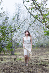 A beautiful young Caucasian woman with curly dark hair walking in blossoming orchard