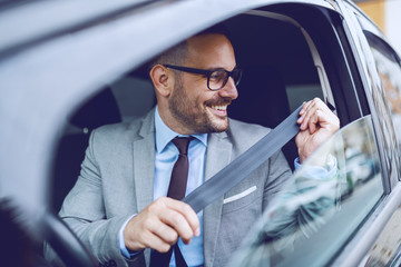Cheerful caucasian businessman buckling seat belt while sitting in his expensive car.