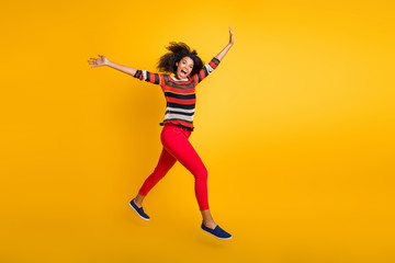 Discounts i come. Full size profile side photo of crazy funky afro american girl jump run want spring weekend bargains wear striped shirt red pants trouser isolated over yellow color background