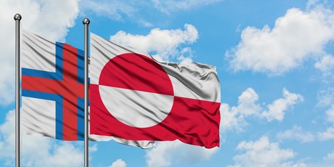 Faroe Islands and Greenland flag waving in the wind against white cloudy blue sky together. Diplomacy concept, international relations.