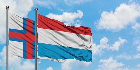 Faroe Islands and Luxembourg flag waving in the wind against white cloudy blue sky together. Diplomacy concept, international relations.