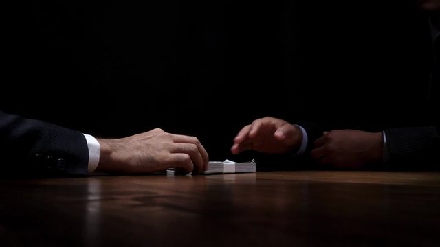 Businessman giving money to partner in dark room after making secret deal, bribery and corruption concepts