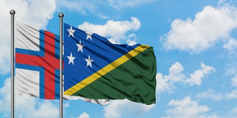 Faroe Islands and Solomon Islands flag waving in the wind against white cloudy blue sky together. Diplomacy concept, international relations.