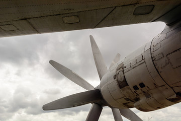 Part of the fuselage of the old military plane with the propeller closeup against the background of an empty and gray sky.