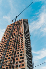 Fototapeta premium Construction of high-rise buildings in the town with tower crane with lifting boom in daytime, vertical