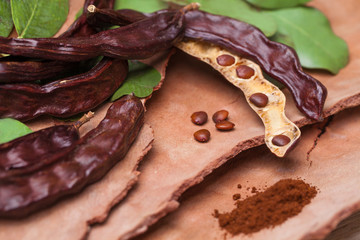 Carob. Organic carob pods with seeds and leaves on tree bark table. Healthy eating, food background.