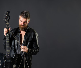 Handsome bearded in leather jacket with electric guitar. Man with beard holds musical instrument. Guitarist in jacket with electric bass guitar. Music party, entertainment. Rock musician with guitar.