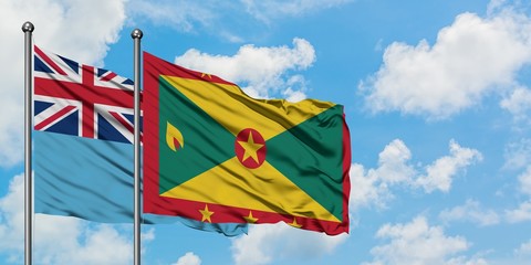 Fiji and Grenada flag waving in the wind against white cloudy blue sky together. Diplomacy concept, international relations.