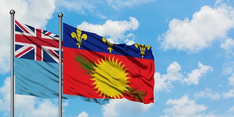 Fiji and Guadeloupe flag waving in the wind against white cloudy blue sky together. Diplomacy concept, international relations.