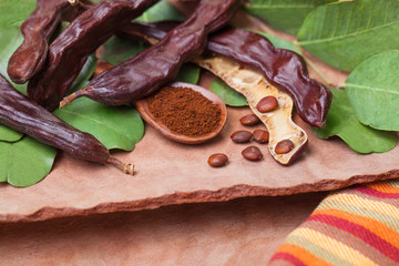Carob. Organic carob pods with seeds and leaves on tree bark table. Healthy eating, food background.