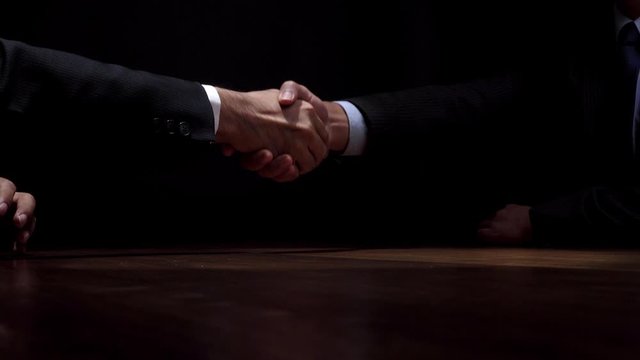 Anonymous business partners making handshake after secret negotiation in dark shadow