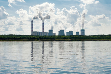 Fototapeta na wymiar Coal-fired power station mirroring in water, with steam billowing from high chimneys in Poland