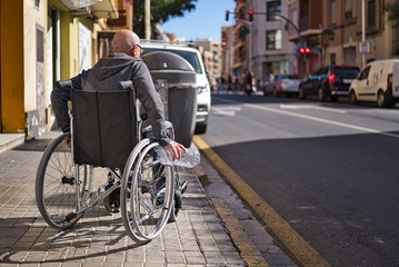 Wheelchair disabled person picking up a transparent plastic bottle thrown and abandoned on the floor to throw it into the garbage recycling container and avoid being contaminated. Avoid plastics