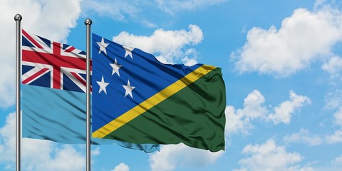 Fiji and Solomon Islands flag waving in the wind against white cloudy blue sky together. Diplomacy concept, international relations.