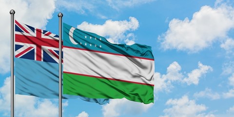 Fiji and Uzbekistan flag waving in the wind against white cloudy blue sky together. Diplomacy concept, international relations.