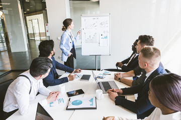 Company leader standing near the flipchart. A team of young businessmen working and communicating together in an office. Corporate businessteam and manager in a meeting