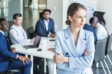 Fototapeta premium Business woman stands on the background of partners. A team of young businessmen working and communicating together in an office. Corporate businessteam and manager in a meeting