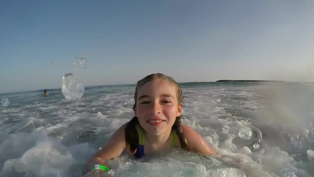 Cheerful girl glides along the wave while lying ona board