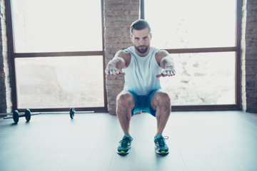 Full length photo of macho guy doing static squats fat burning sportswear white tank-top blue shorts sneakers training at house home studio near big windows indoors