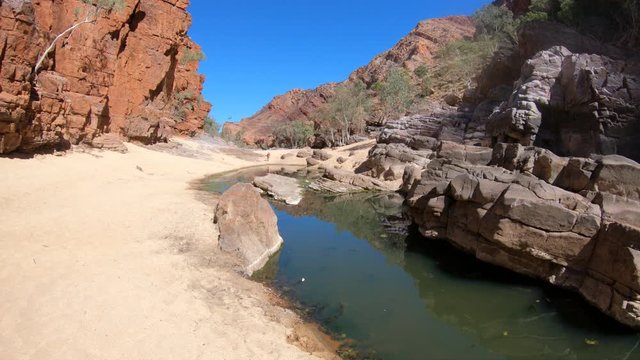 Aerial view of rugged rocky cliffs of Ormiston Gorge in West MacDonnell Range National Park reflected in a pool on the river in dry season. Northern Territory, Central Australia, Outback Red Centre.