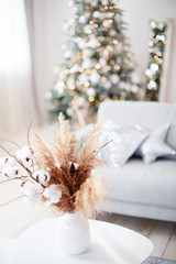 Christmas decorations. Cozy interior in pastel colors. Cotton branches in a vase on a table. Multi-colored bokeh in the background
