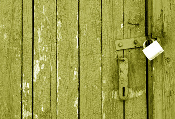 Grungy wooden door with lock in yellow tone.