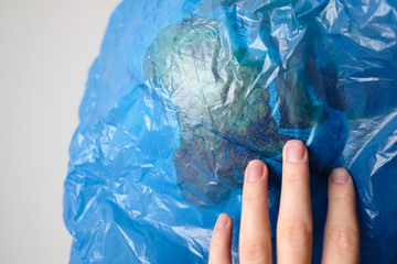 World globe in a blue plastic bag. Environmental pollution. The planet is in danger. The human hand is trying to save the world