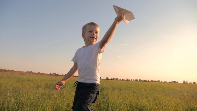 happy family childhood a slow motion video concept. little boy runs across the field with a paper airplane playing a pilot. happy child holds paper lifestyle plane